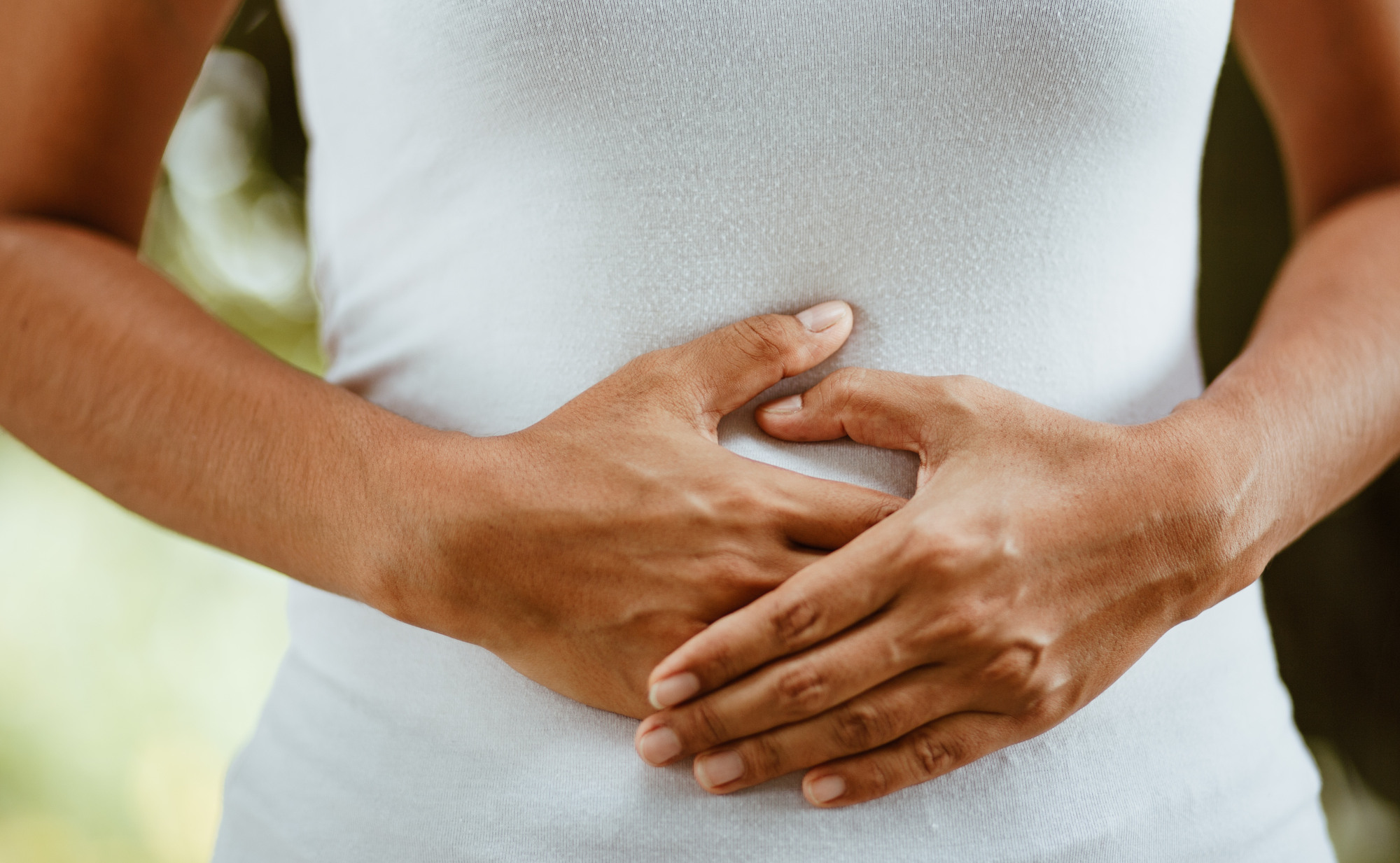 Eine Frau in einem weißen, enganliegenden Shirt hält ihre Hände auf ihren Bauch. Ein Symbolfoto für die besondere Verbindung zwischen Bauch und Kopf.