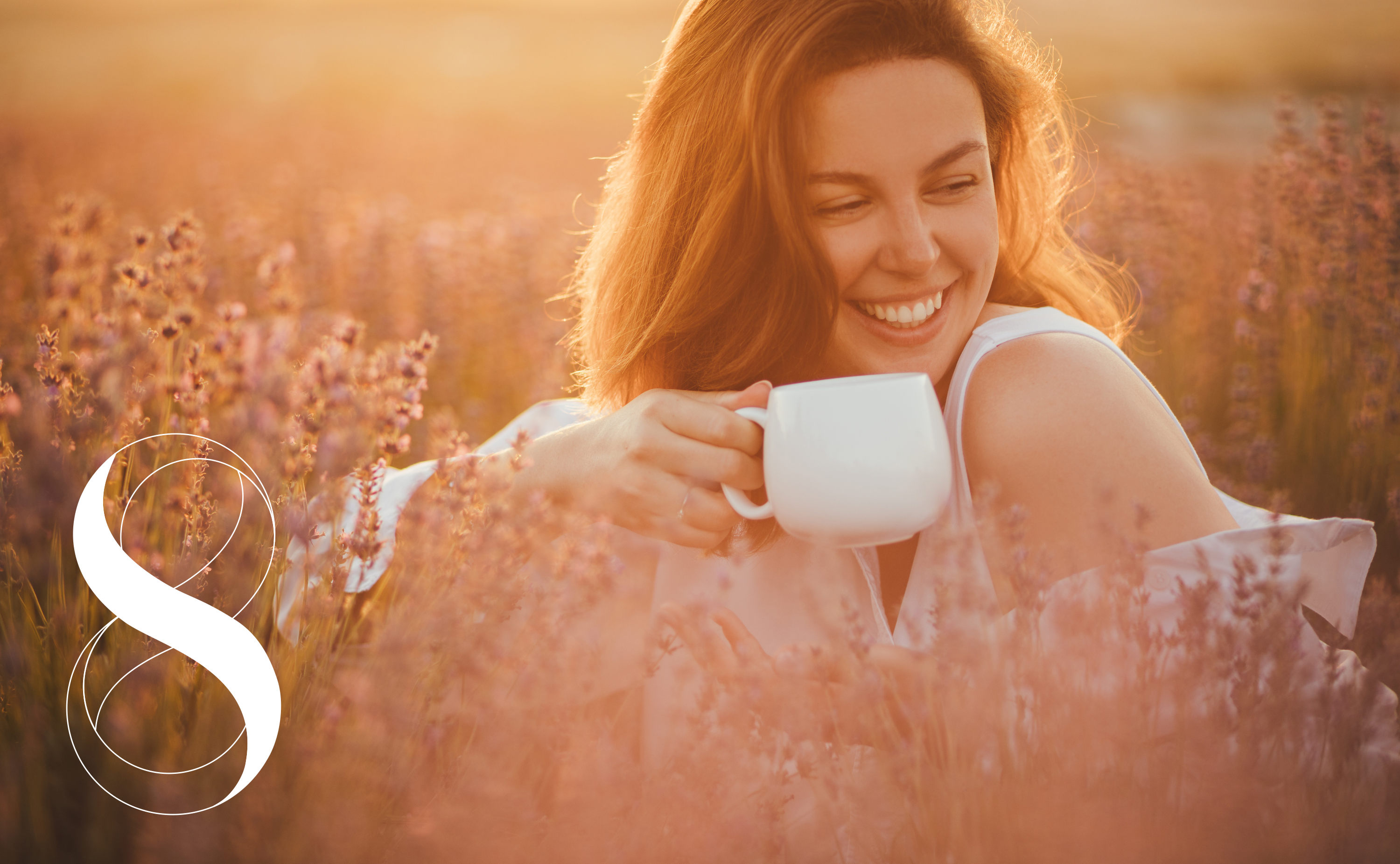 Eine lachende Frau sitzt bei Sonnenuntergang in einem Feld voller Kräuter und hält eine Tasse in den Händen. Ein Symbolfoto für die Kraft fermentierter Kräuter.