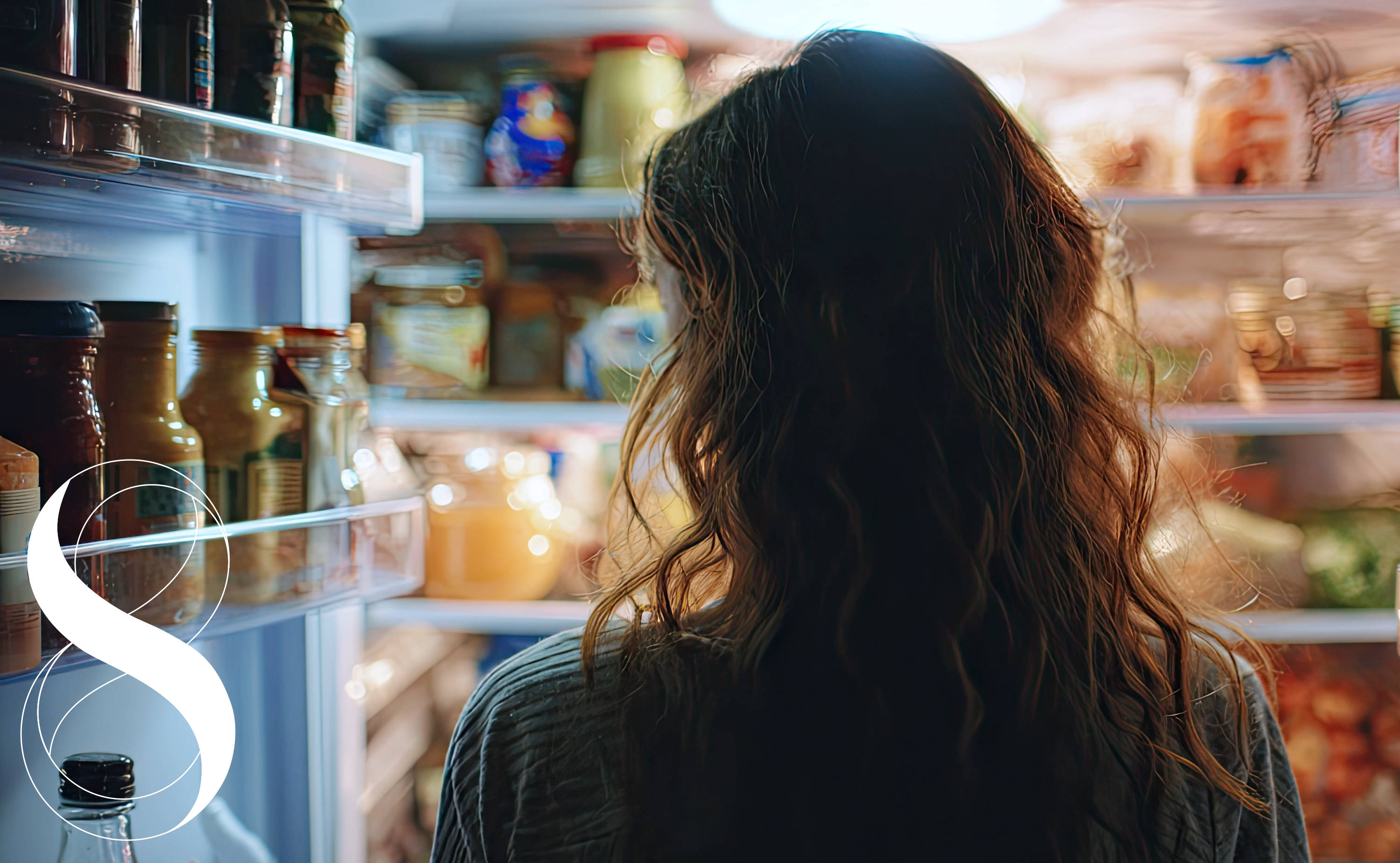Foto einer Frau von hinten mit welligem Haar, die in einen hell beleuchteten, offenen Kühlschrank schaut. Die Regale sind voller Lebensmittel, Gläser, Flaschen und Saucen. In der unteren linken Ecke befindet sich das 8-Elements-Logo von Life Light.
