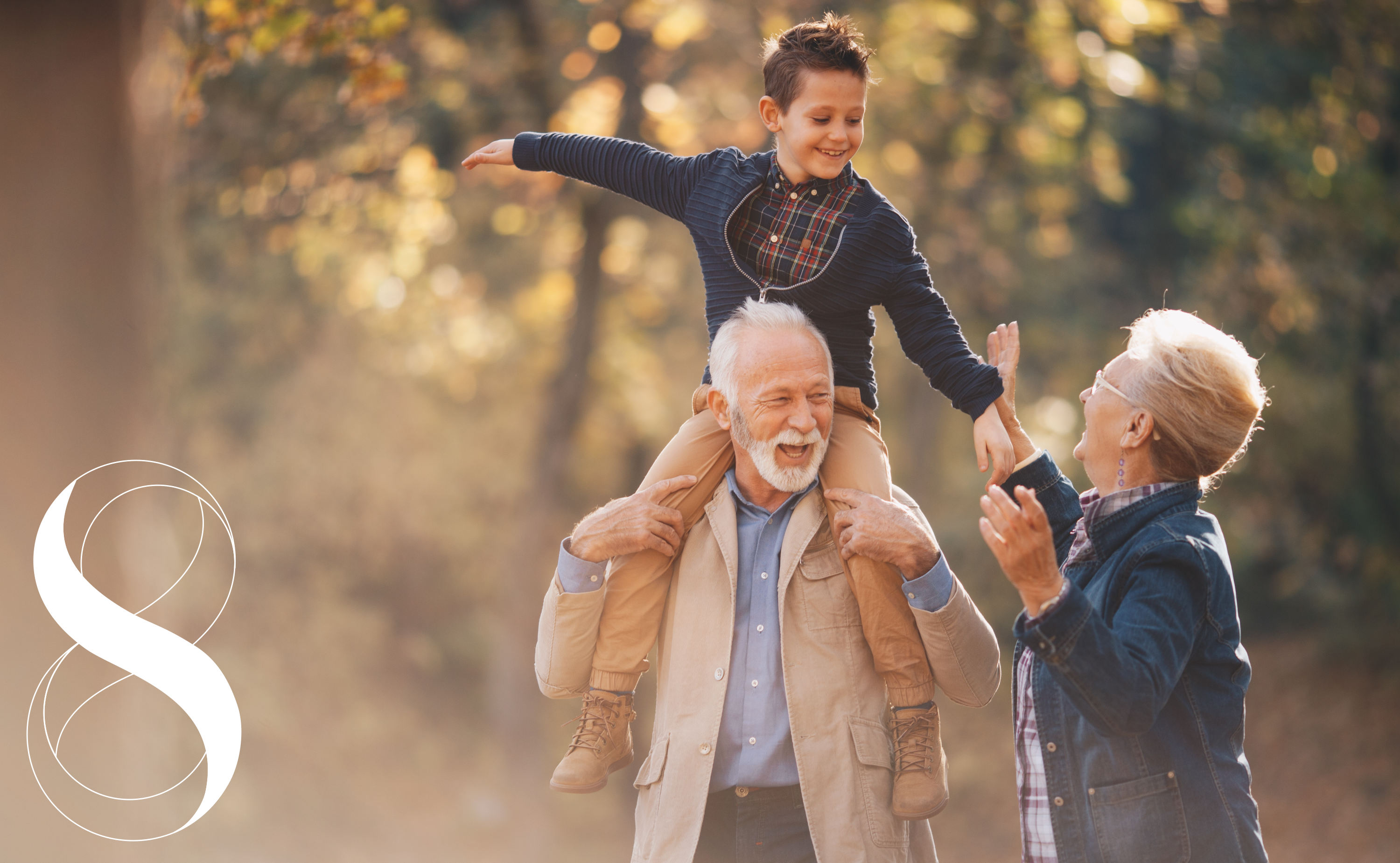 Großeltern und Kind im Herbstwald: Ein Kind sitzt auf den Schultern des Großvaters, während sich die Großmutter daneben zum Kind hochstreckt und lacht. ein Symbolbild von LIFE LIGHT für Longevity und gesundes Älterwerden.
