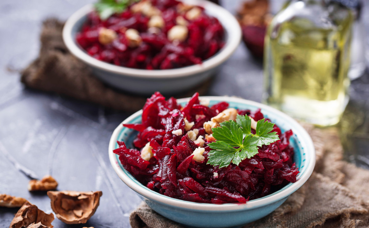 Frisch geraspelter Rote-Bete-Salat in einer Keramikschale, garniert mit Walnussstücken und Petersilie.