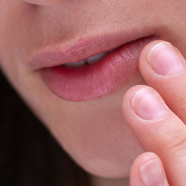 Nahaufnahme der Lippen eines Menschen, der mit dem Finger sanft die Lippe berührt.