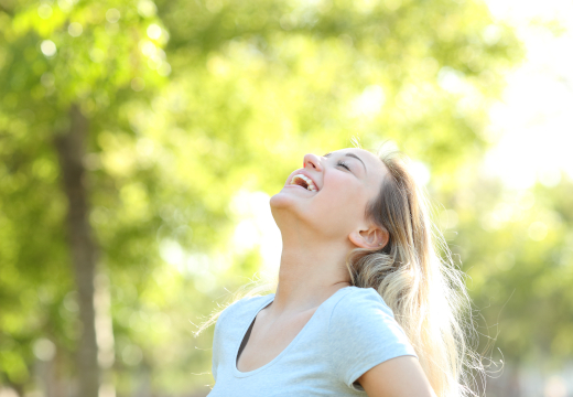 Eine junge Frau atmet tief im Freien vor unscharfem, sonnigem Grün. Ein Symbolfoto von LIFE LIGHT für freies Durchatmen und gesunde Atemwege.